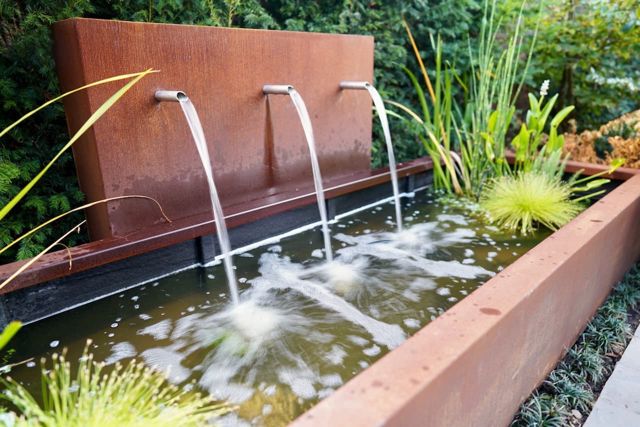 Corten steel water wall with three cascading spouts into a raised pond