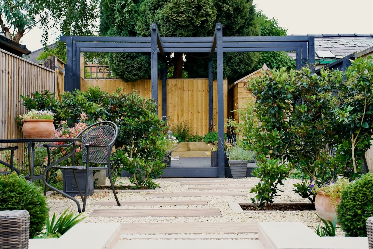 Timber pergola over a dining table on diamond-pattern stone paving