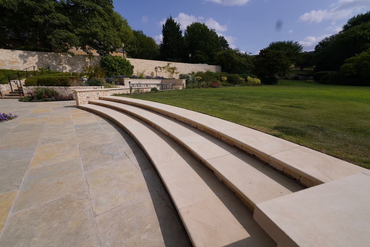 Curved honey-stone amphitheatre steps leading up to a formal lawn